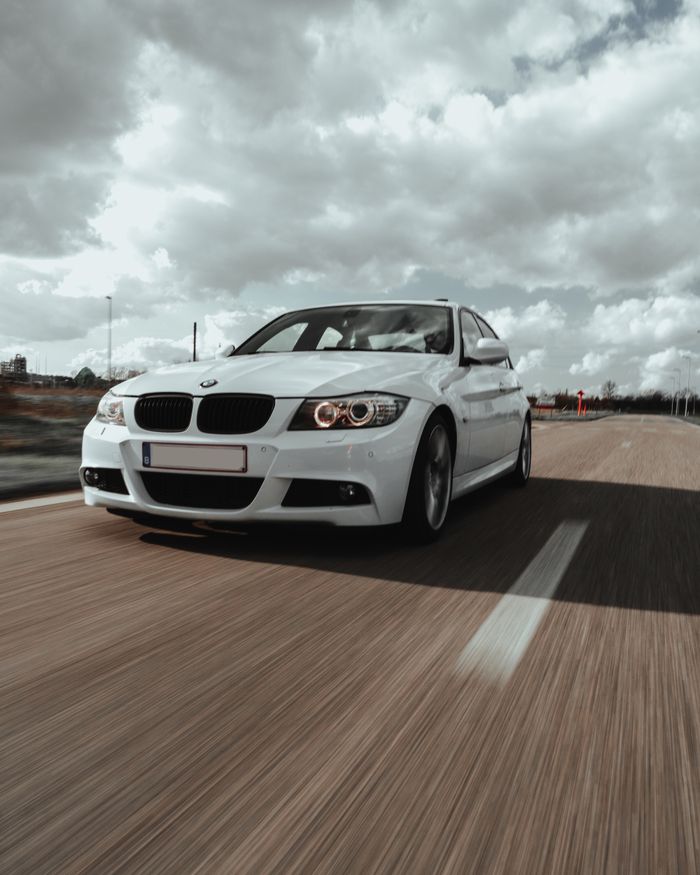About Dynamic shot of a white sedan driving on an open road under a dramatic cloudy sky.
